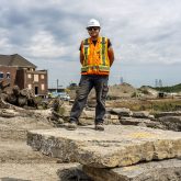 Person in construction gear stands on flat rock smiling.
