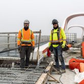 Two people in construction work on a bridge.