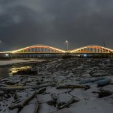 A bridge over a snow-covered riverbank, lit up at night.