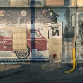 A weathered painted mural of a fire truck on a building with boarded up windows.