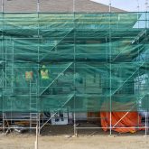 Green mesh surrounding scaffolding around the outside of a building.