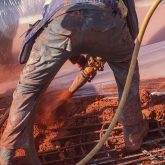 A worker controlling a hose spraying red concrete.