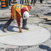 Construction worker measuring a flat concrete circle.