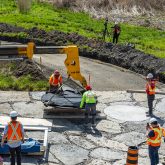 Construction workers moving a piece of equipment covered in a black tarp.