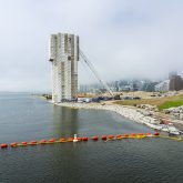 A large industrial crane surrounded by scaffolding and fabric on the side of a river.