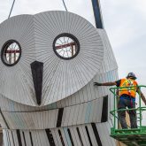 A worker on a lift pushing the owl's head into position.