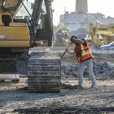 A worker cleaning mud from the wheels of an excavator with a shovel.