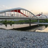 View of a modern white and red bridge reflected in the water, at sunset with clear sky.