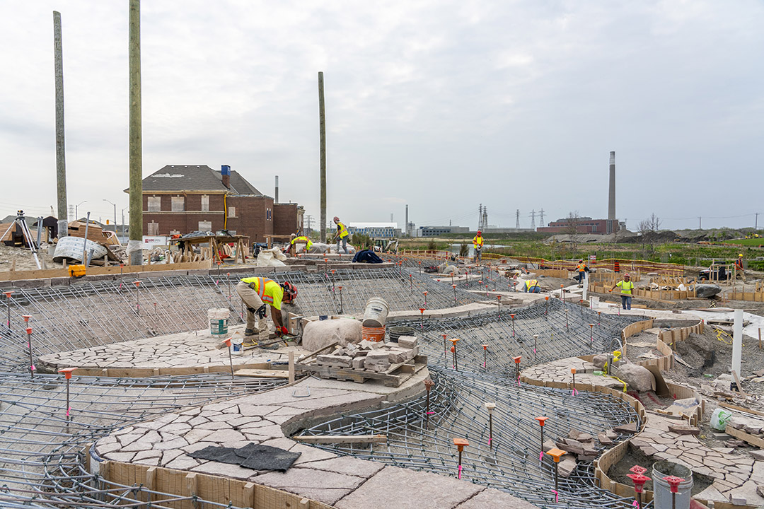 A worker standing on a strip of paving stones between areas that look like they are covered by steel rebar nets. 