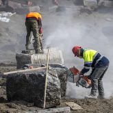 Two construction workers sawing into boulders.