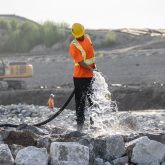 A construction worker spraying rocks with a hose.