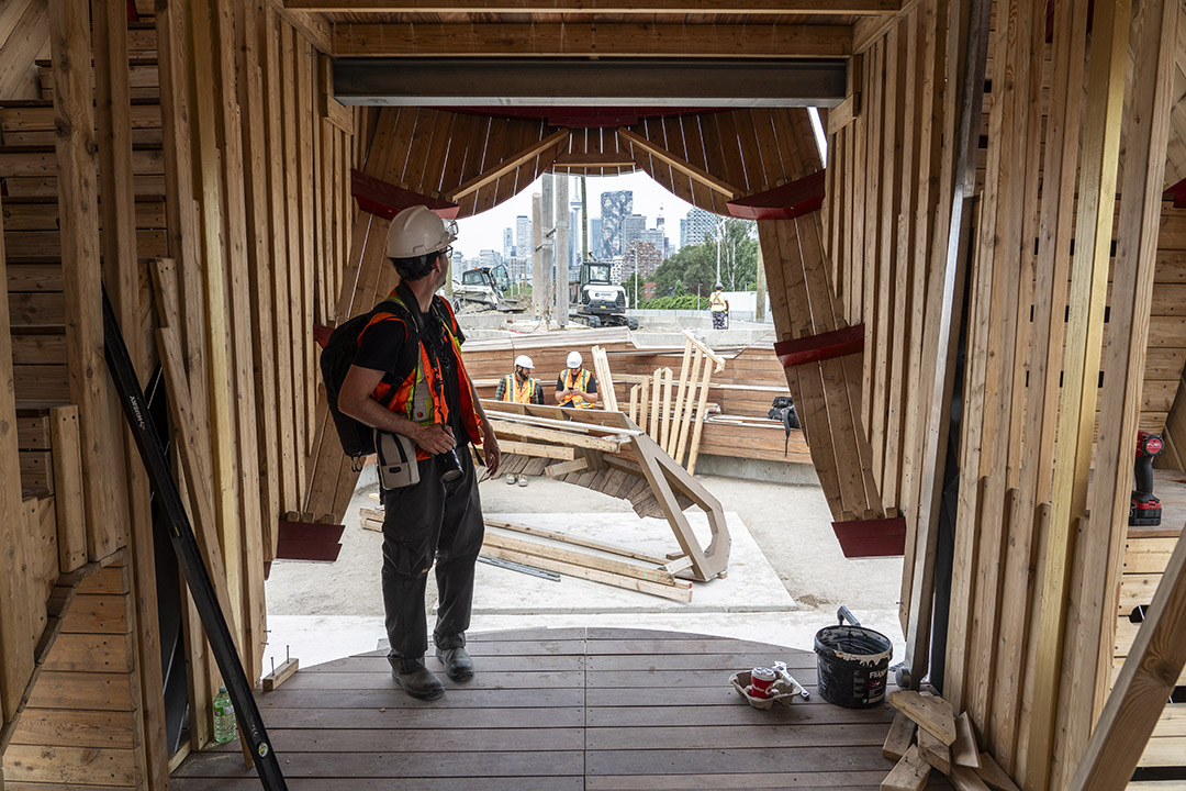 A man standing on a stage looking out through the wooden 'curtains'. 
