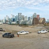 A construction site with pickup trucks in front of mounds of soil.