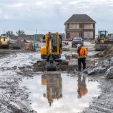 A worker and an excavator standing behind a large puddle.
