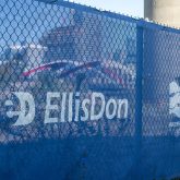 Construction site banners displaying the logos of EllisDon and seen through a chain-link fence.