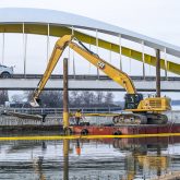 An excavator on a barge in front of a bridge