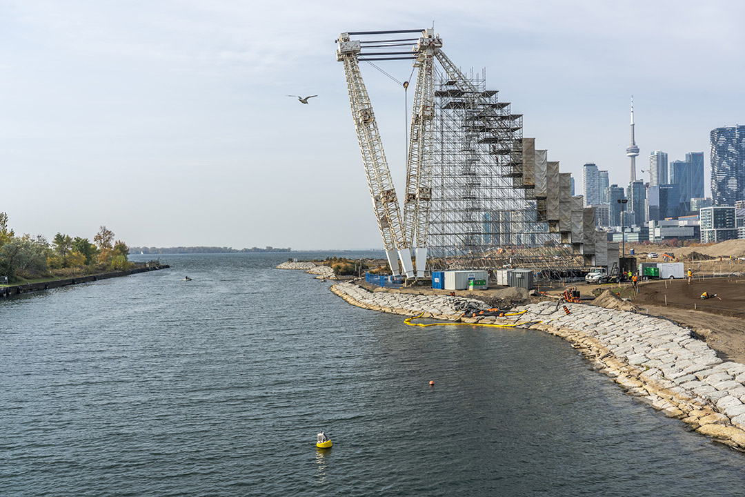 An industrial crane on the edge of a lake. The crane is partly covered in scaffolding.