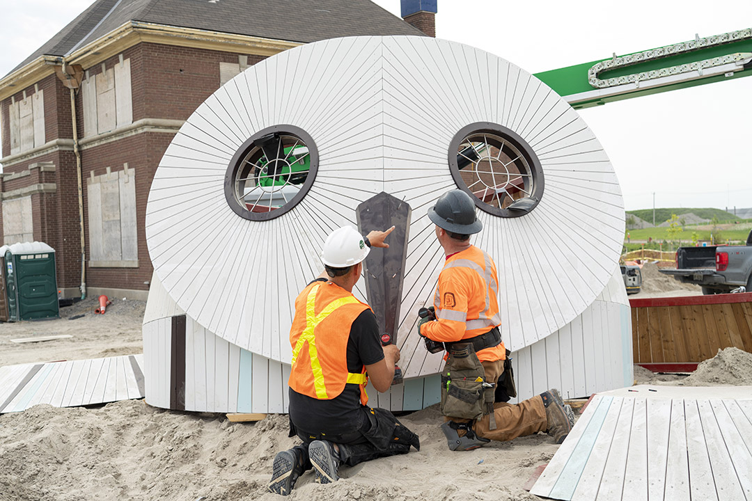 Workers kneeling in front of a giant owl head.